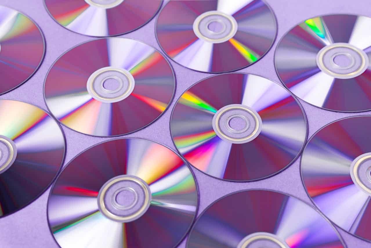 A close-up view of multiple shiny compact discs (CDs), arranged in a circular pattern, reflecting light in different colors