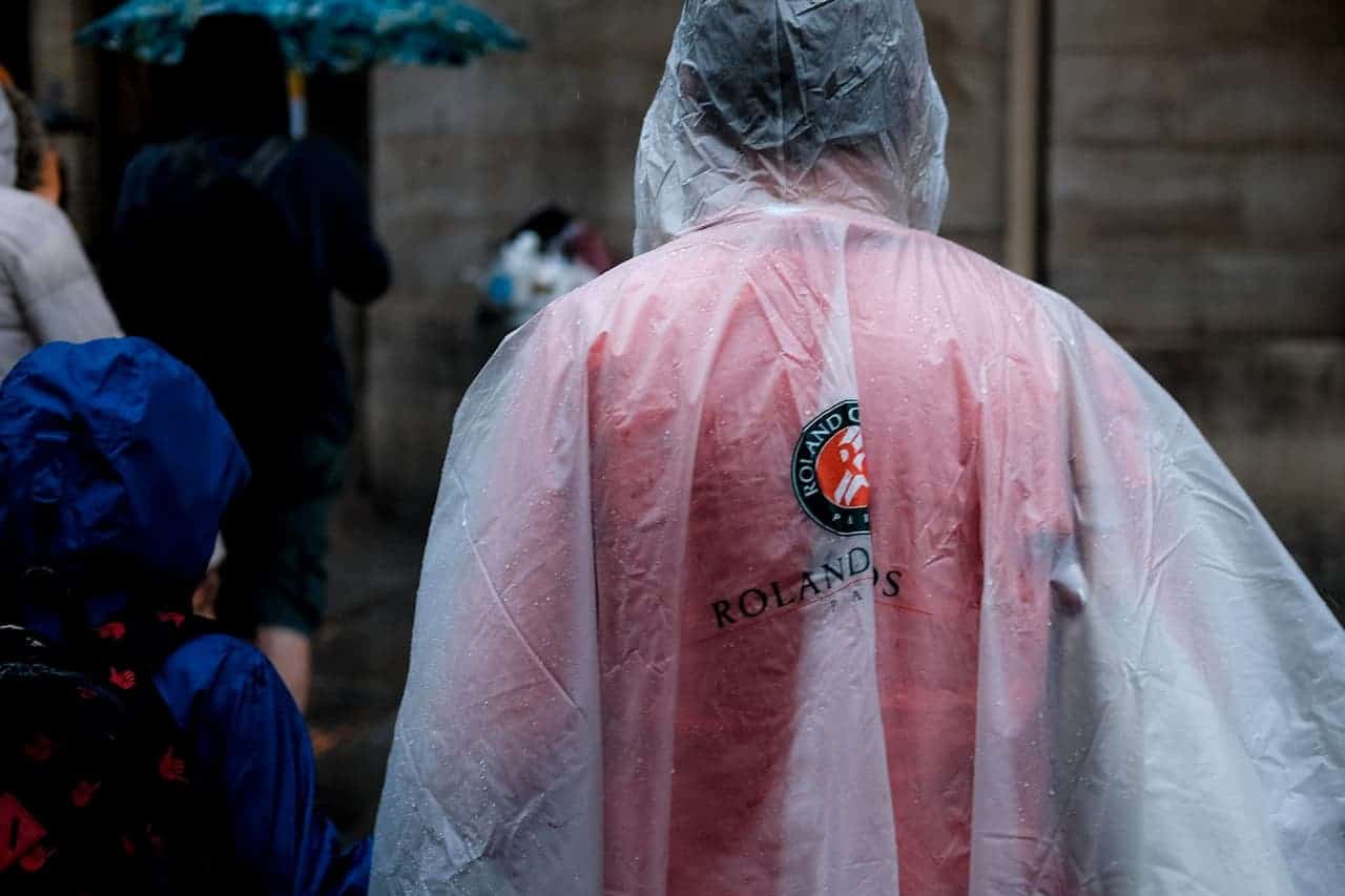 Person wearing transparent rain poncho over Roland Garros tennis outfit, seen from behind in rainy weather conditions