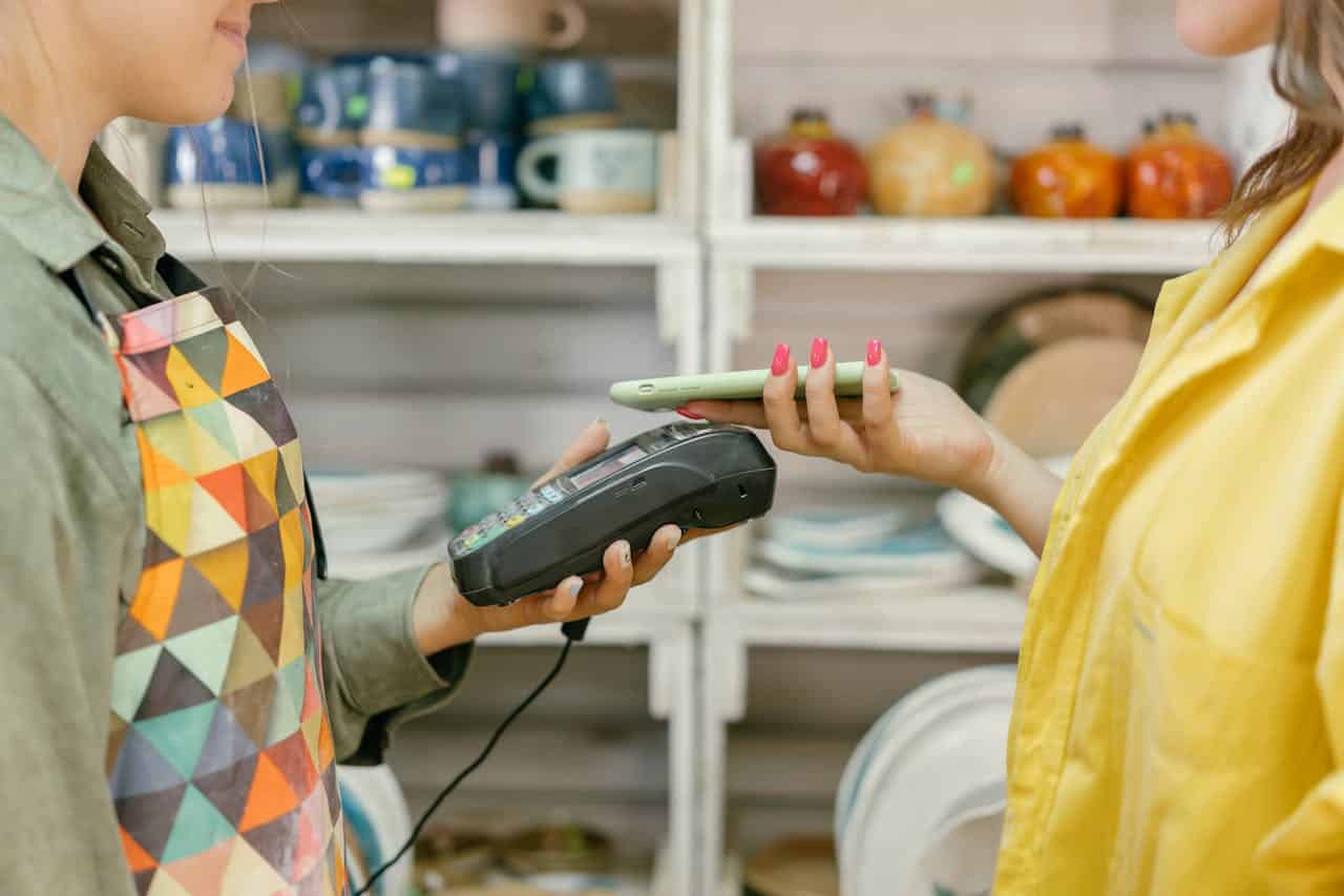 A customer using a smartphone for contactless payment at a store, a cashier holding the card reader machine, paying with mobile payment, modern shopping experience, store transaction