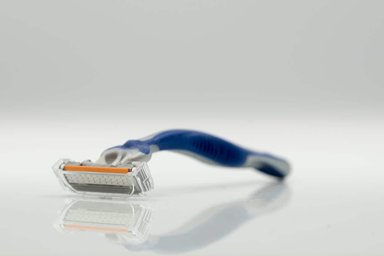 Razor with a blue handle, placed flat on a reflective surface, close-up of the razor blade, shaving tool for personal grooming, sharp razor edge visible