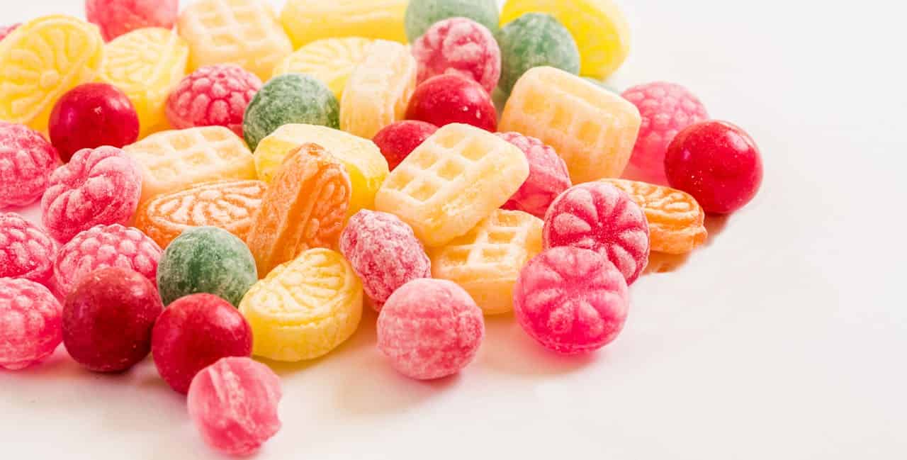 Colorful assorted hard candies, red, green, yellow, orange, and pink, various shapes, some resembling raspberries