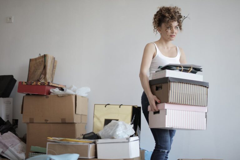 Woman holding stacked storage boxes, organizing clutter, preparing for decluttering, cleaning or moving, sorting personal items, indoor home organization, managing belongings, tidying up living space