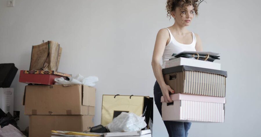 Woman holding stacked storage boxes, organizing clutter, preparing for decluttering, cleaning or moving, sorting personal items, indoor home organization, managing belongings, tidying up living space