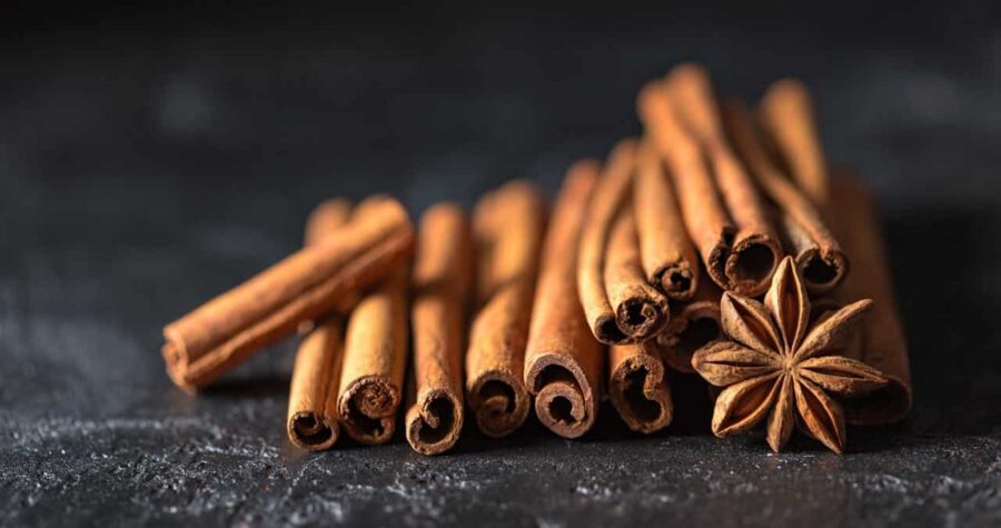 A pile of cinnamon sticks and a star anise sit on a dark surface, cinnamon sticks are arranged in a stacked pattern, star anise is placed at the center, showcasing their texture and shape