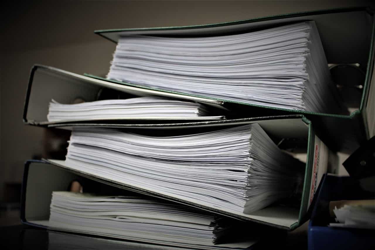 Stacks of filing binders filled with paper documents, neatly organized, business or office setting, heavy paperwork, multiple binders