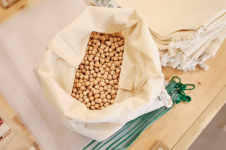 Dried chickpeas, placed on a wooden surface, reusable cloth bags stacked nearby, eco-friendly and sustainable packaging