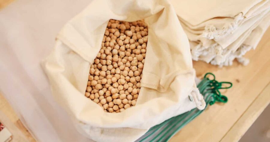 Dried chickpeas, placed on a wooden surface, reusable cloth bags stacked nearby, eco-friendly and sustainable packaging