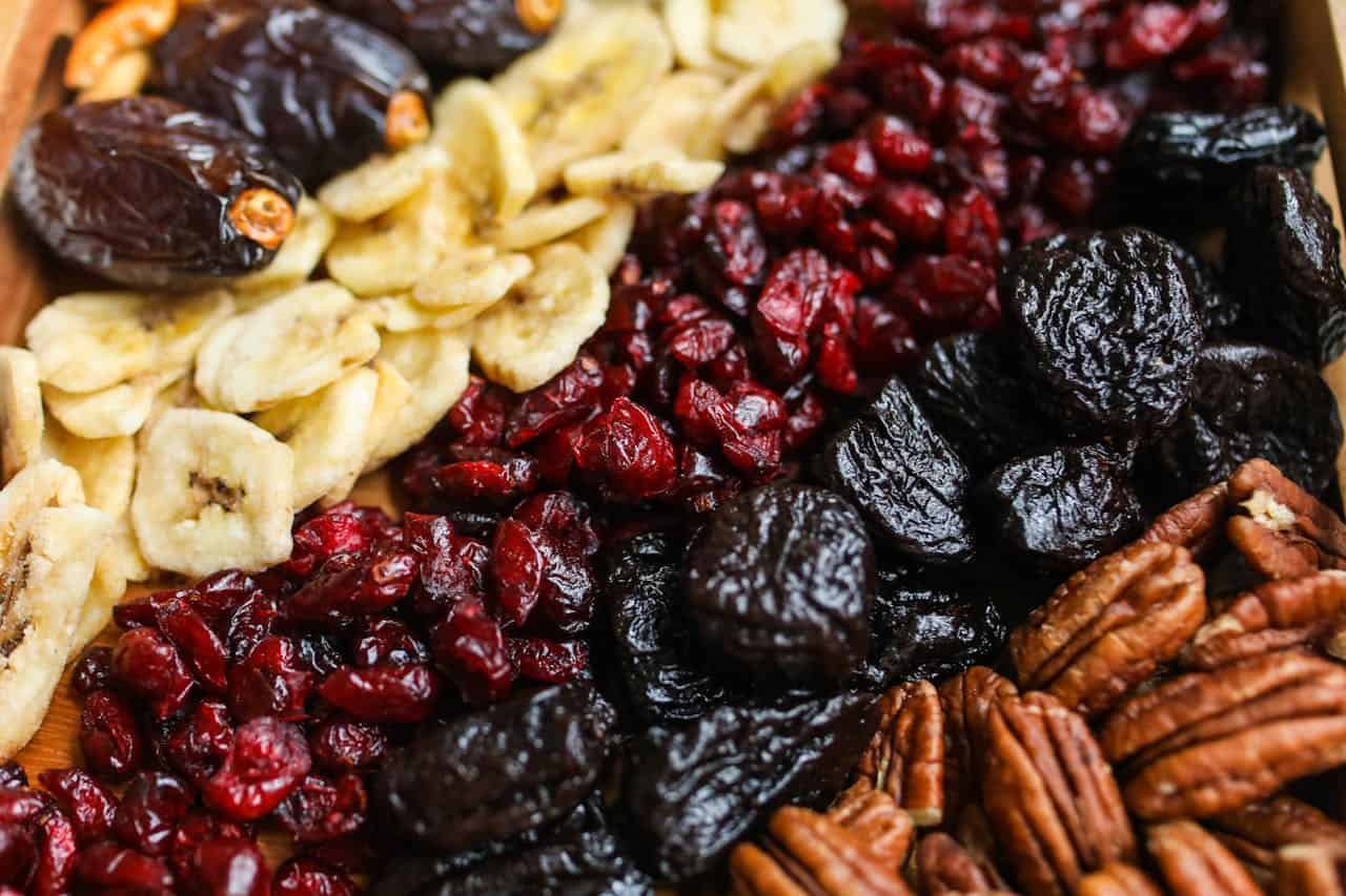 Assorted dried fruits and nuts, including dates, banana chips, dried cranberries, prunes, and pecans, rich in fiber and nutrients