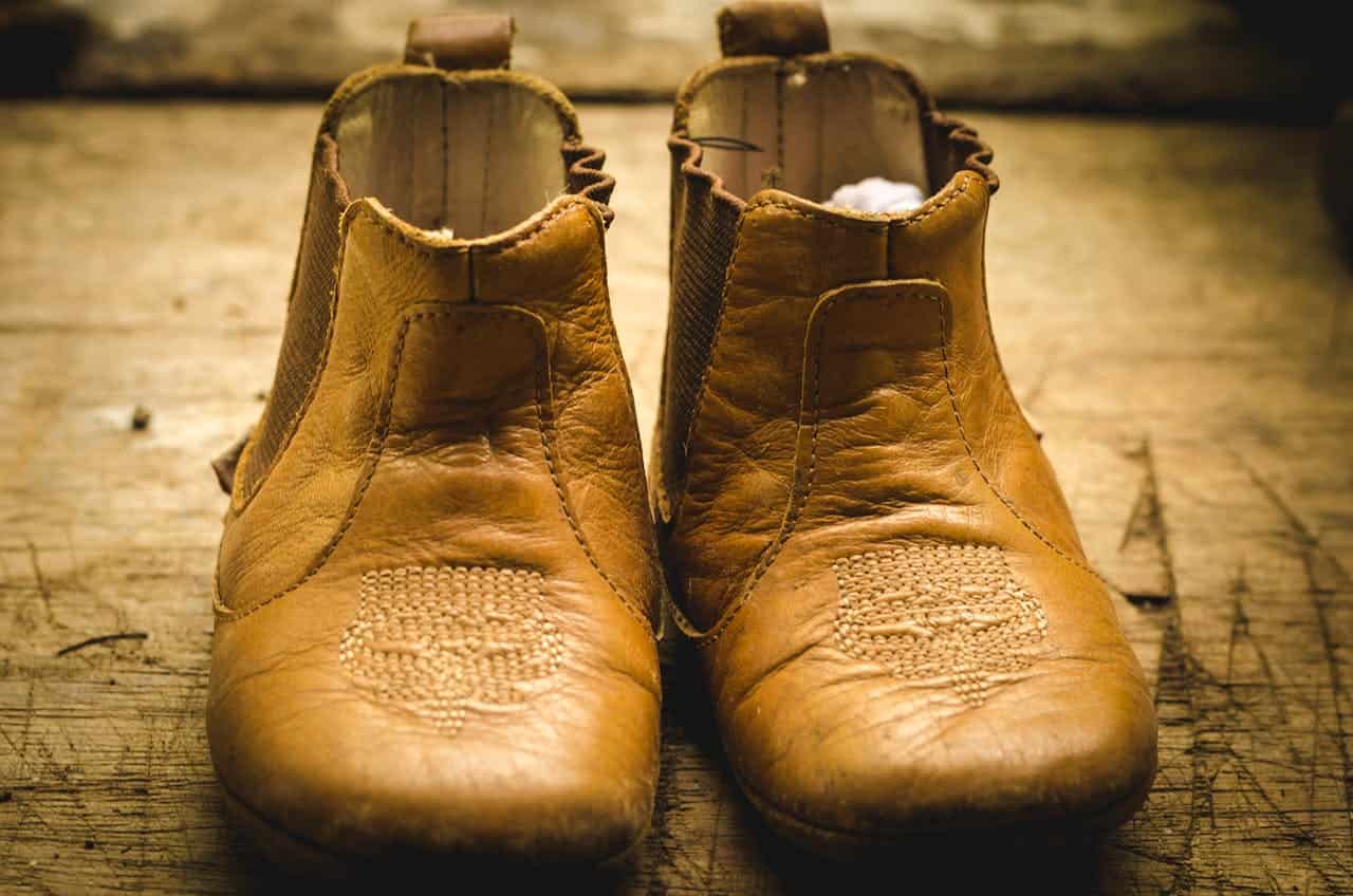 A pair of well-worn brown leather shoes, the shoes have a worn texture and detailed stitching, displayed on a wooden surface, showing a rustic, aged appearance