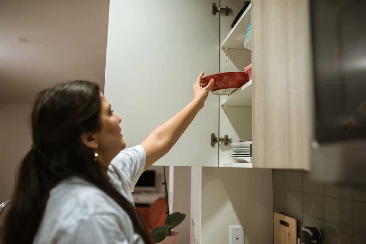 Person putting back a red bowl, organizing kitchen cabinet, storing items in kitchen, home organization, kitchen tasks, domestic chores