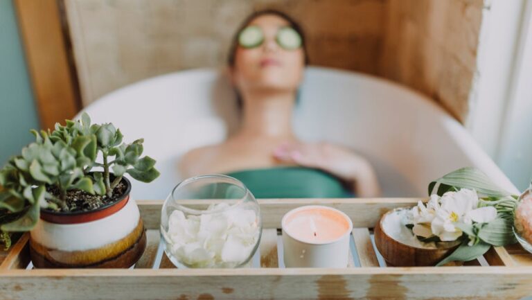 A woman relaxing in a bath with cucumber slices on her eyes, a wooden tray with a candle, rose petals, a plant, and flower petals in a bowl placed beside the bath, peaceful and serene spa-like setting, the focus on self-care and relaxation