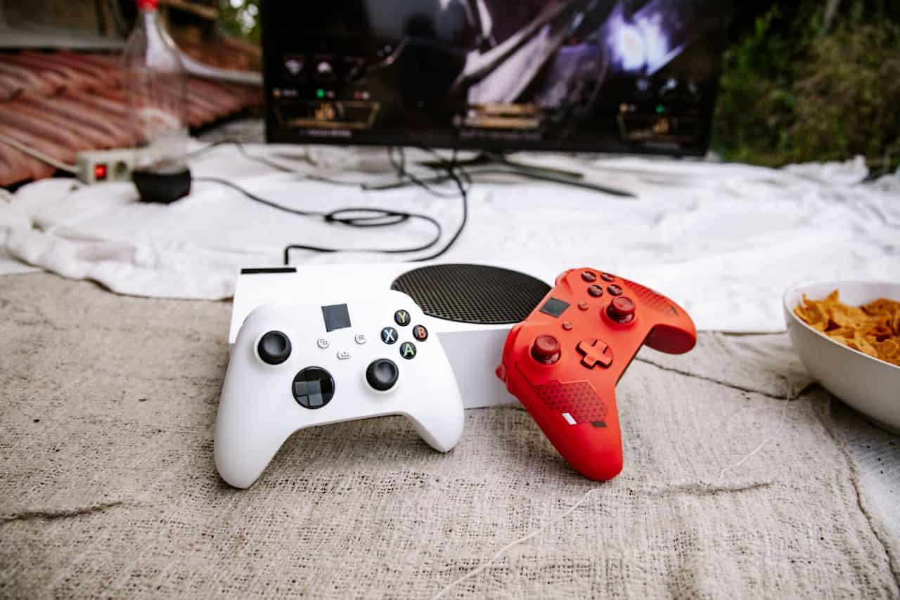 Gaming setup with white and red controllers, Xbox console, television displaying gameplay, snacks in a bowl, casual indoor environment, relaxing gaming session