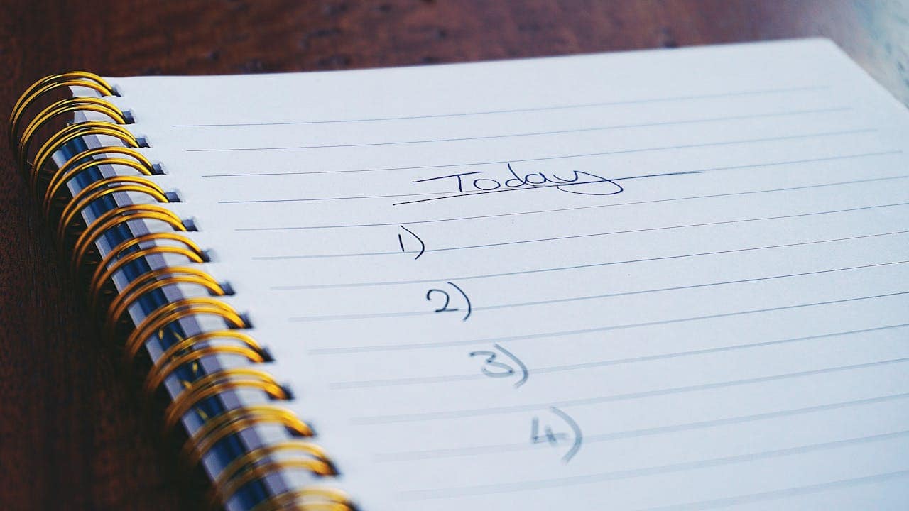 A close-up of an open notepad, titled "Today," with numbered lines for a to-do list, visible gold spiral binding, clean white paper, inviting organization, empty lines for writing tasks or goals