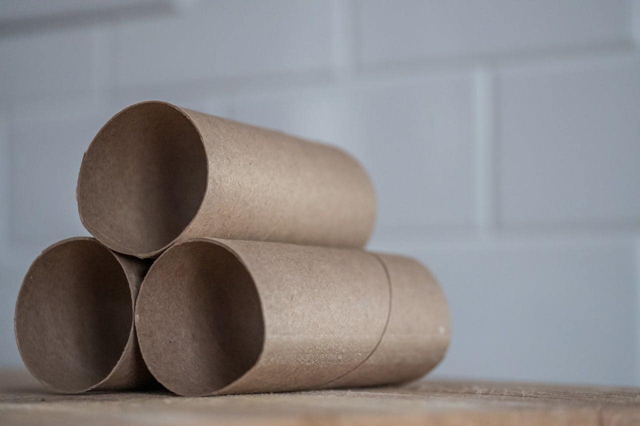 Three empty brown cardboard tubes stacked in a triangular arrangement, set on a wooden surface, with a blurred white background