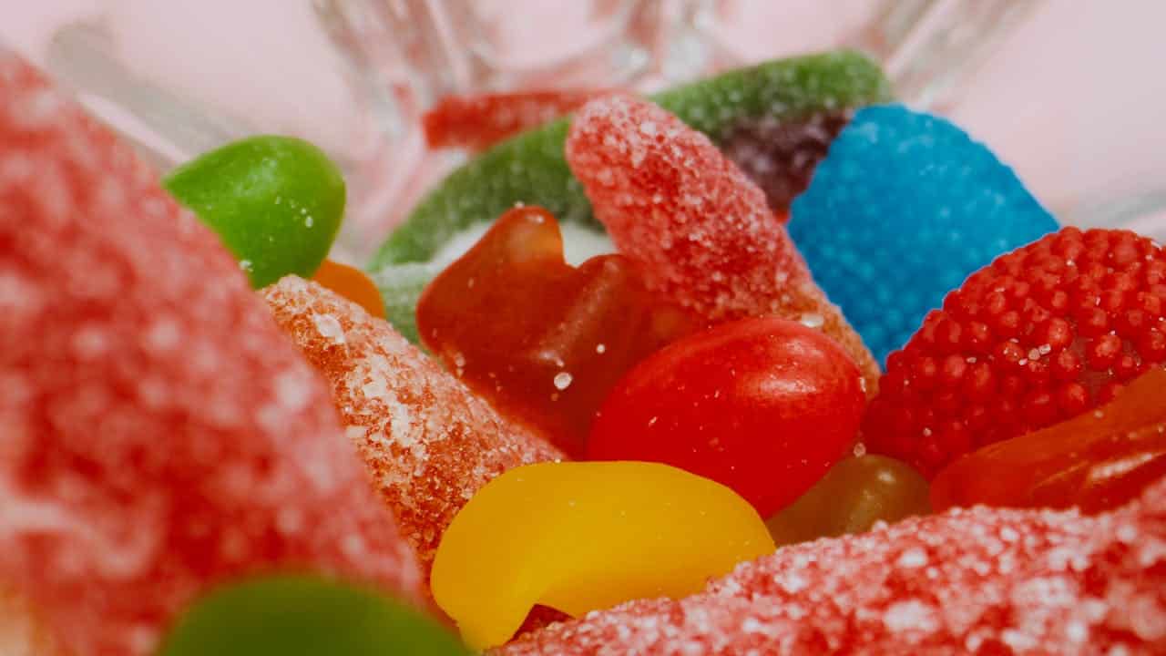 Brightly colored gummy candies, red, green, yellow, and blue, sugar-coated texture, close-up shot, vibrant candy assortment, sweet, chewy treats, in a glass bowl, various shapes and sizes, enticing candy display, perfect for snacking, tempting sweet treats