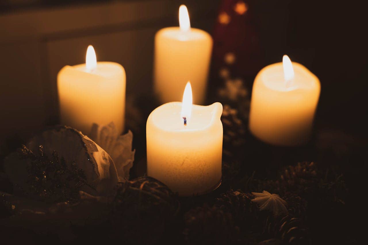 Four lit candles with melted edges, providing a warm glow in a dark setting, acting as a substitute light source, flames flickering gently, useful for power outages, emergencies, or low-light environments