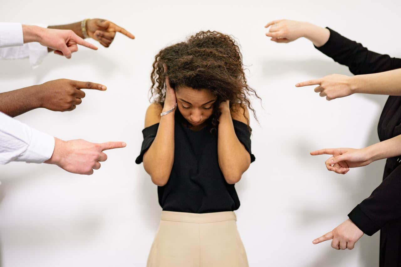 A woman covering her ears, multiple hands pointing at her, indicating judgment or blame, expressions of accusation, feeling overwhelmed or criticized, isolation, dramatic portrayal of social pressure