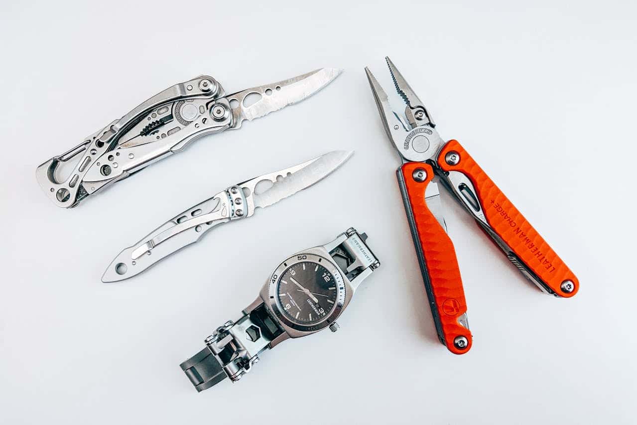 Leatherman tools featuring three folding knives, a metal wristwatch, and orange-handled multi-tool pliers on white background