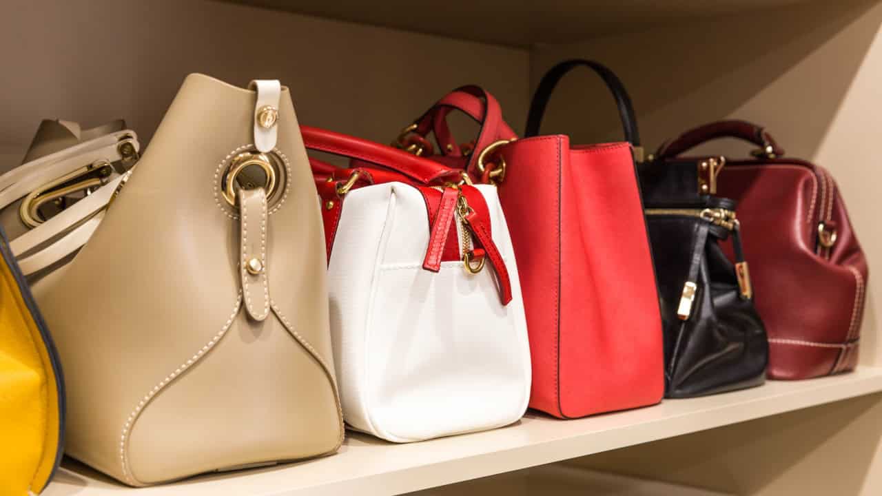 The image shows a collection of handbags in various colors, including beige, white, and red, neatly arranged on a shelf, showcasing different styles and designs for storage