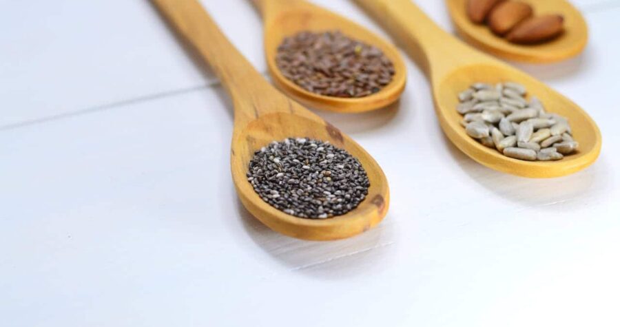 Wooden spoons filled with chia seeds, flaxseeds, sunflower seeds, and almonds, arranged on a white surface, healthy superfoods, natural ingredients, nutrition-rich seeds