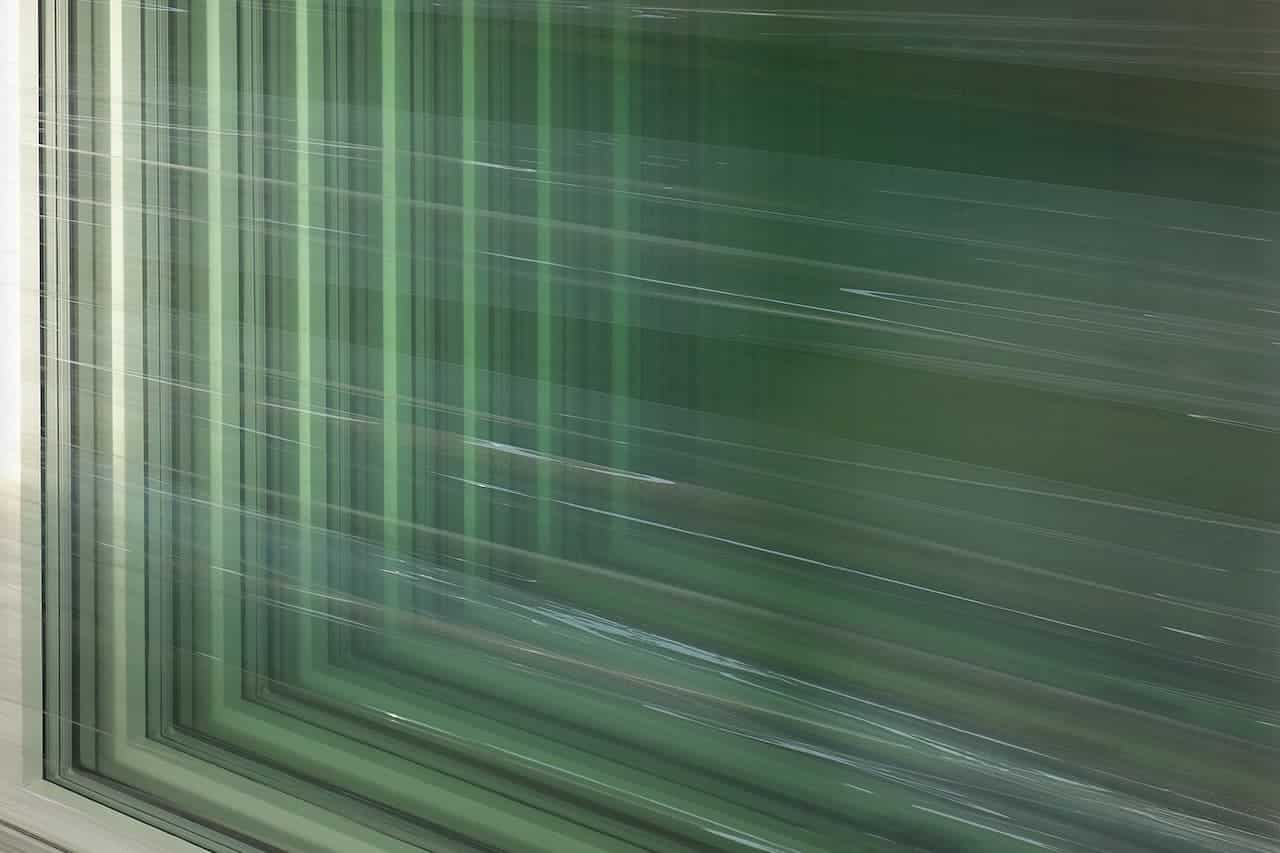 Stacked green-tinted window panes wrapped in clear plastic, showing layered reflections and vertical light streaks across the glass surfaces