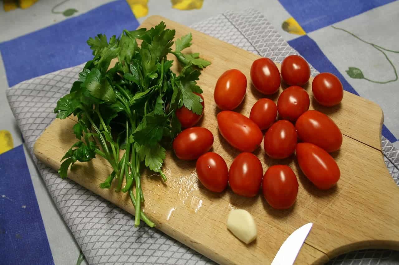 Fresh cherry tomatoes and parsley arranged on wooden cutting board with garlic clove and knife edge visible
