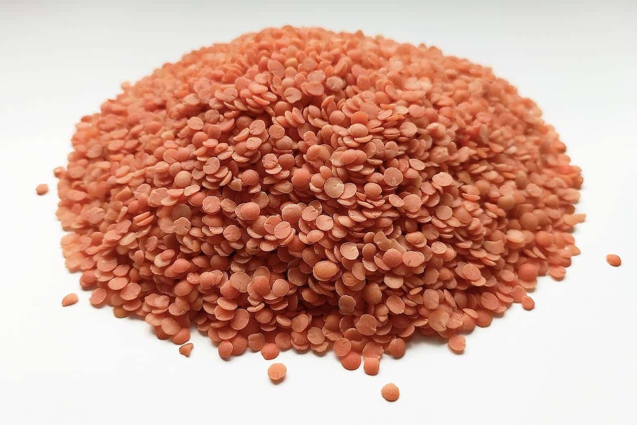 Pile of uncooked red lentils on white surface, showing small disc-shaped legumes with characteristic orange-pink color.