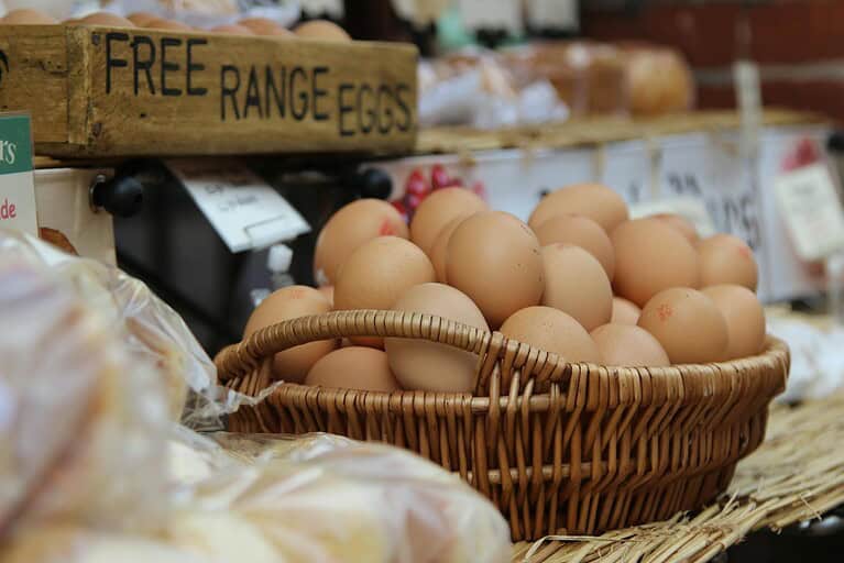 Brown eggs in wicker basket at market stall with wooden "FREE RANGE EGGS" sign visible above display