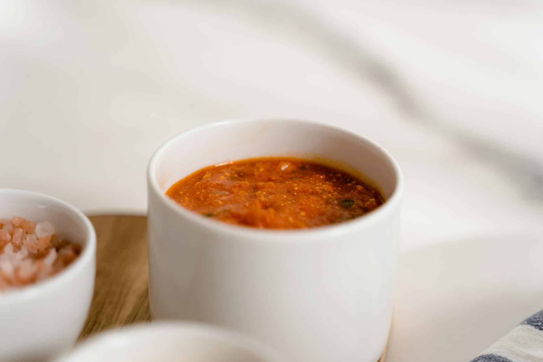 A close-up of rich marinara sauce in a white ceramic cup, perfect for pasta dishes.