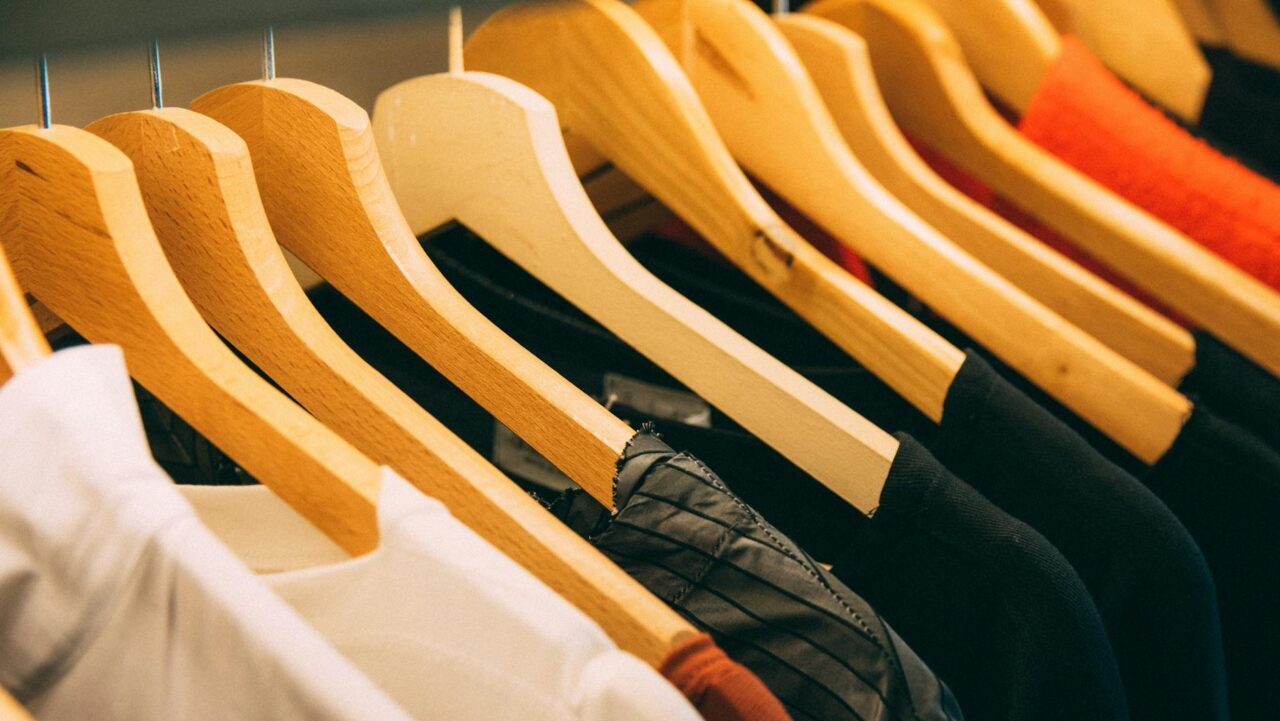 A close-up view of a row of clothes on wooden hangers, showcasing various fabrics and colors in a wardrobe setting.