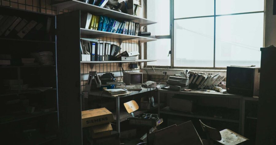 A cluttered, abandoned office space filled with vintage technology and scattered binders.