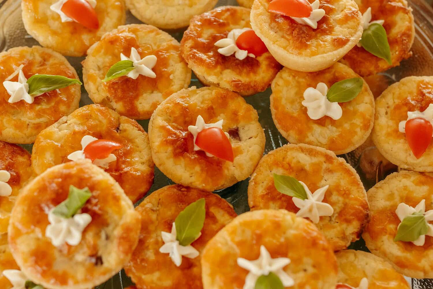A delectable assortment of mini quiches topped with fresh herbs and cheese garnishes.