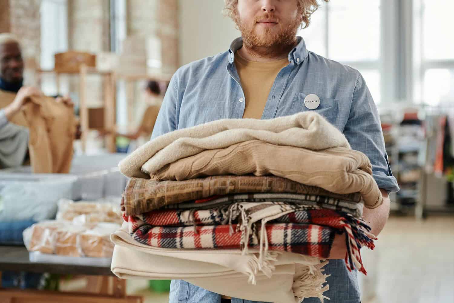 A man holding blankets at a community volunteer event, indoors, during the day.