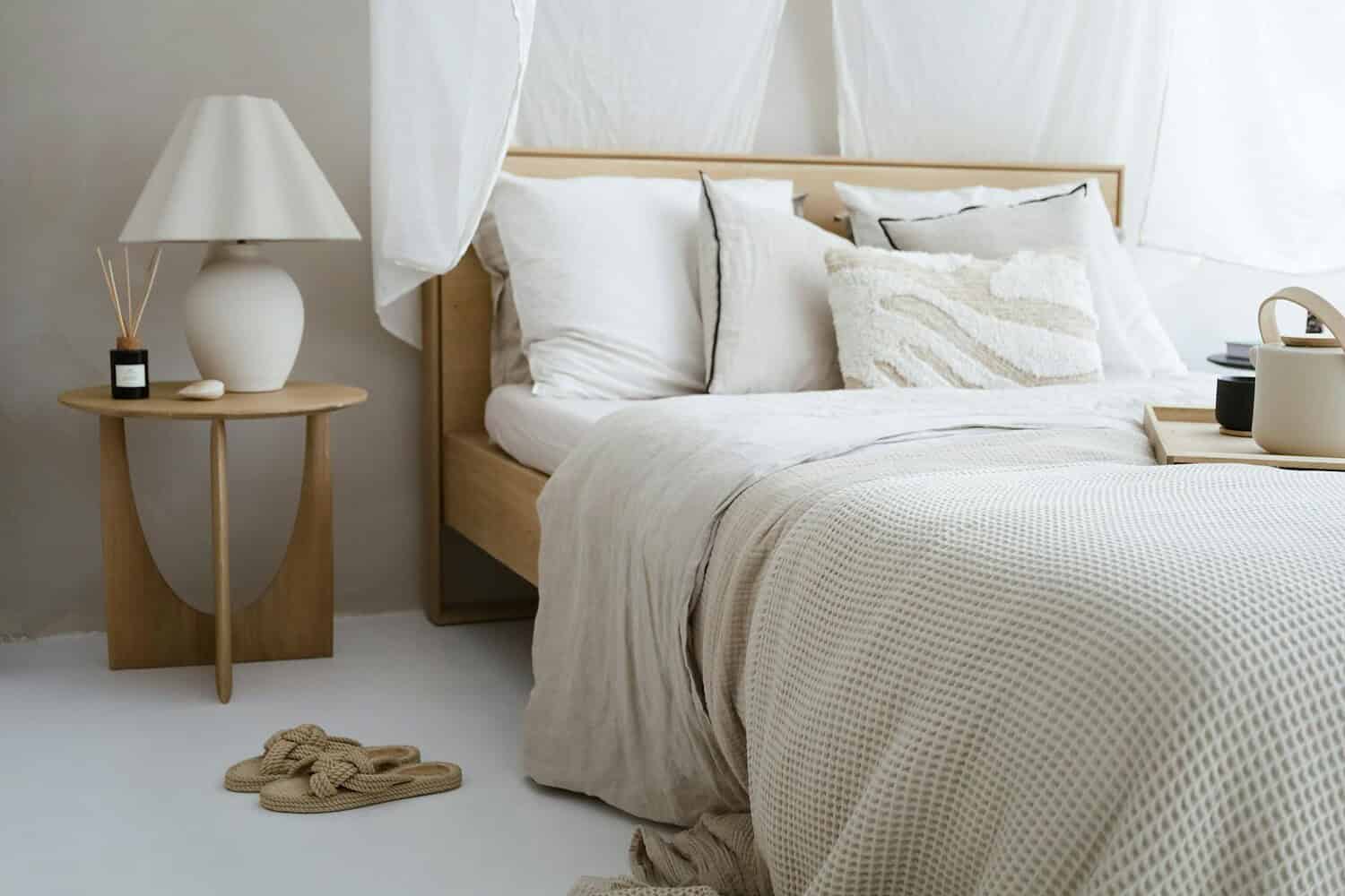 A minimalist bedroom with neutral tones featuring cozy bedding, a side table, and soft lighting.