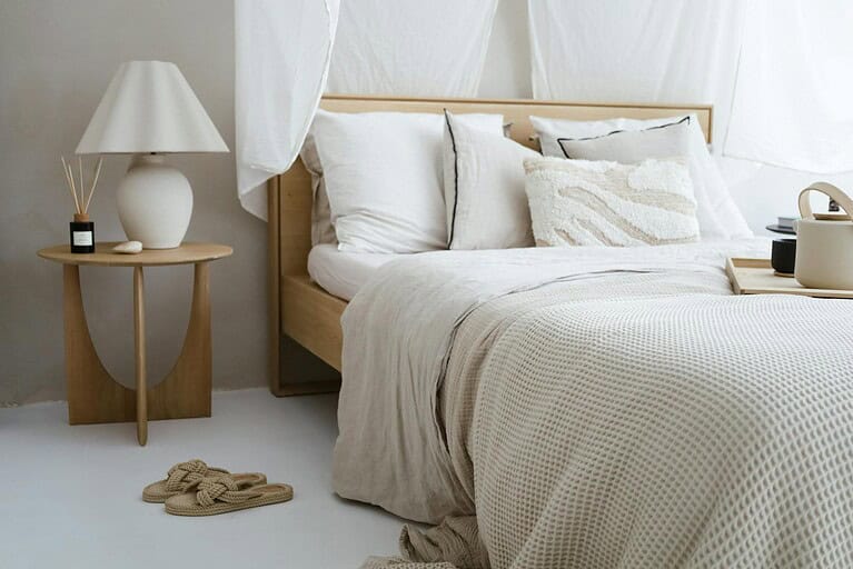 A minimalist bedroom with neutral tones featuring cozy bedding, a side table, and soft lighting.