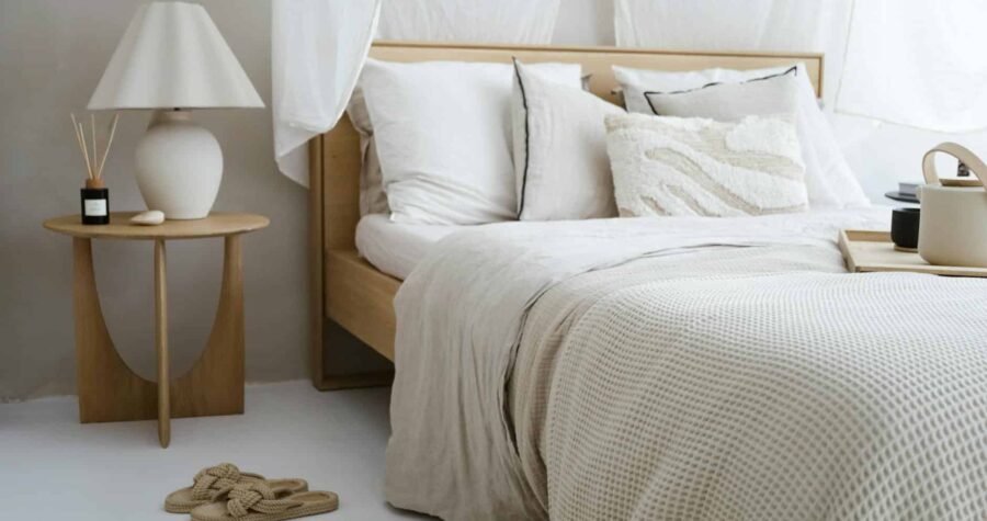 A minimalist bedroom with neutral tones featuring cozy bedding, a side table, and soft lighting.