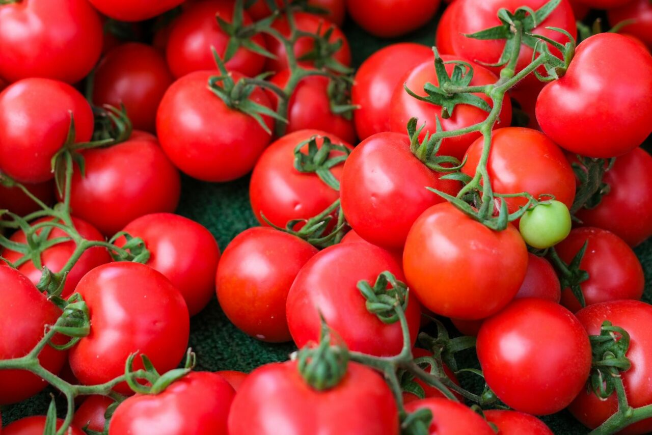 Close-up of bright red cherry tomatoes on the vine, with green stems and one unripe green tomato visible