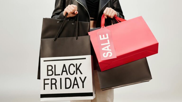 A woman in a leather jacket holds Black Friday shopping bags indoors. Perfect for sale promotions
