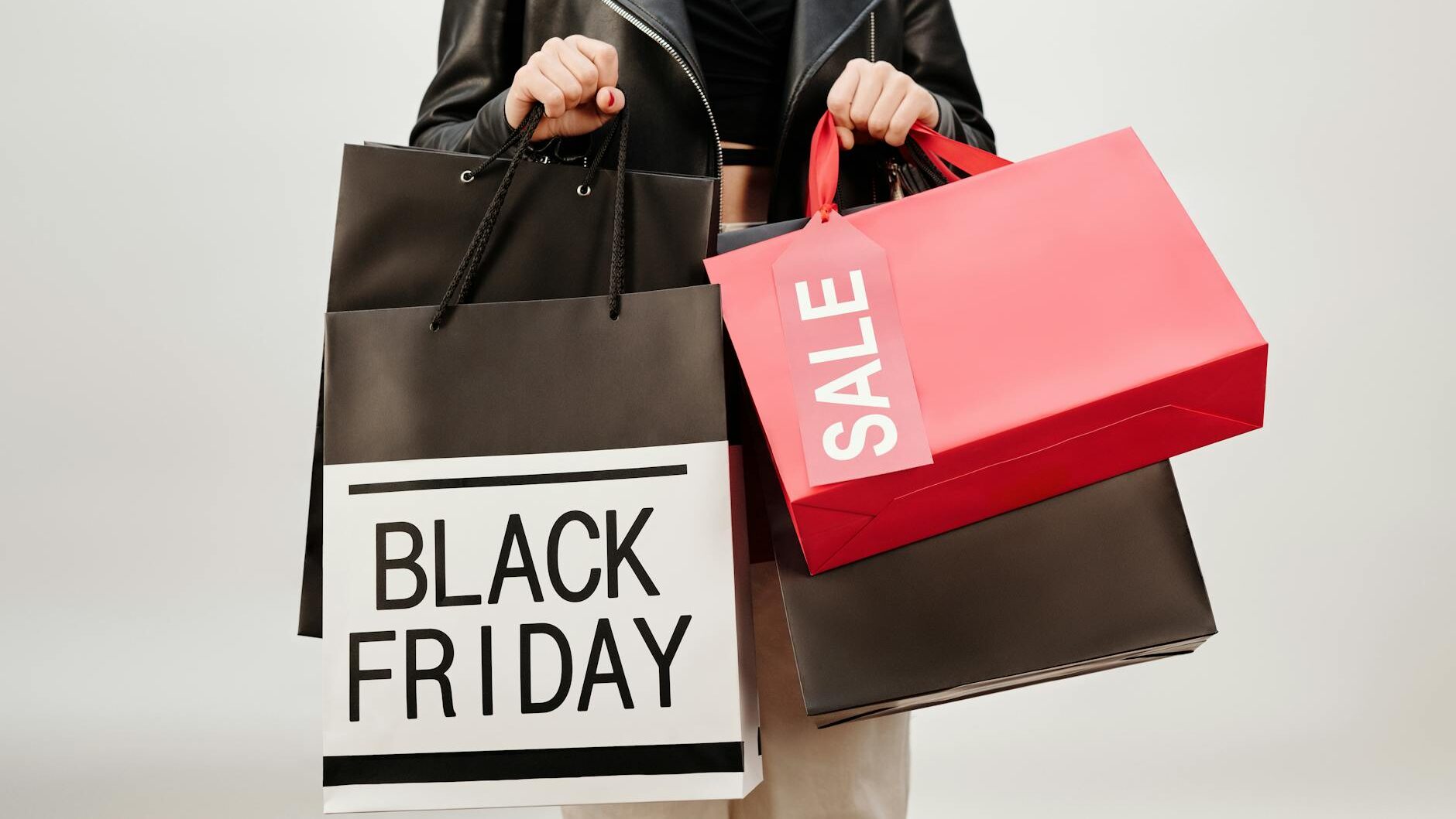 A woman in a leather jacket holds Black Friday shopping bags indoors. Perfect for sale promotions