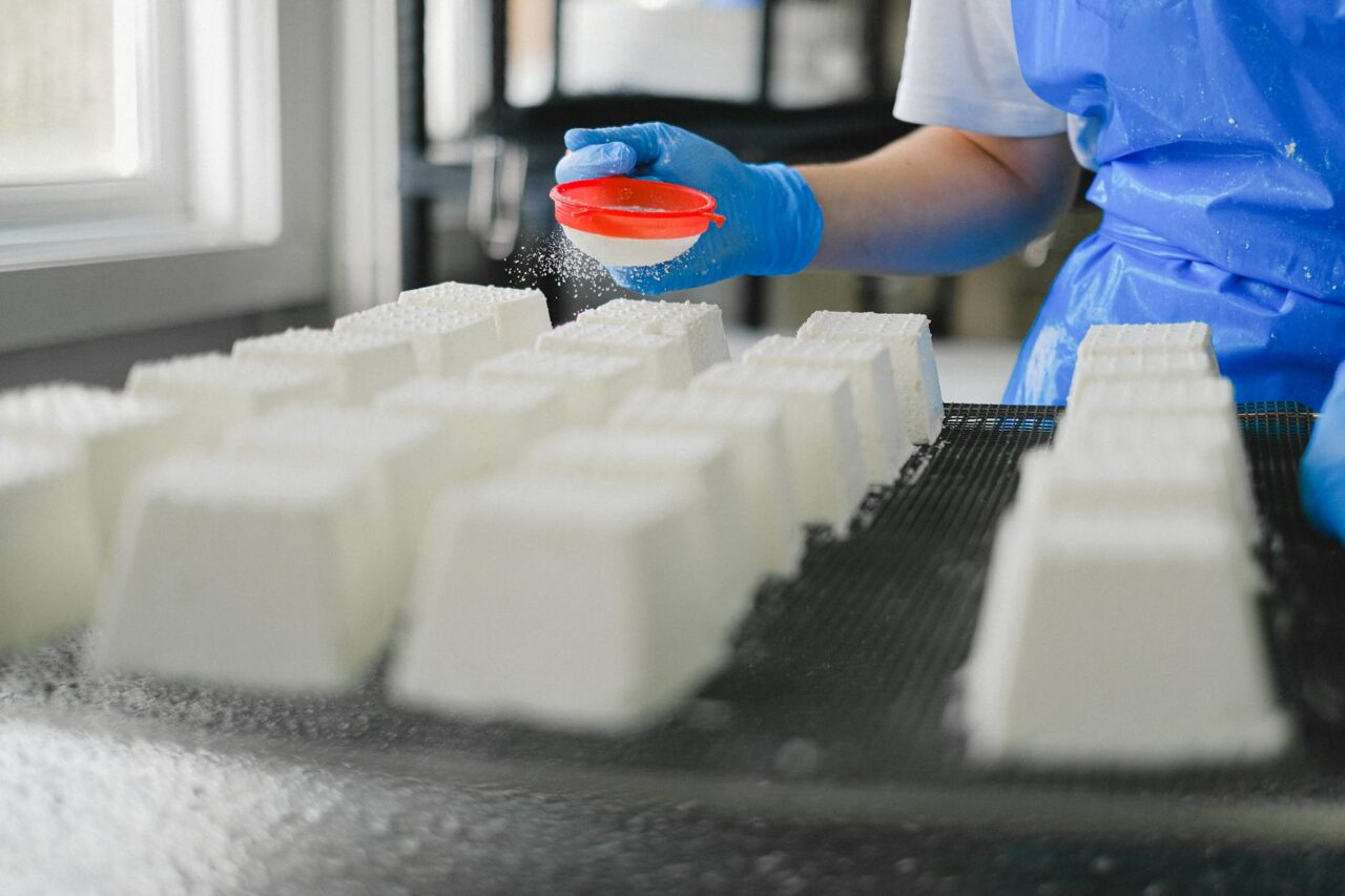 Close-up of a worker wearing gloves, sprinkling cheese in a factory environment, showcasing precision.