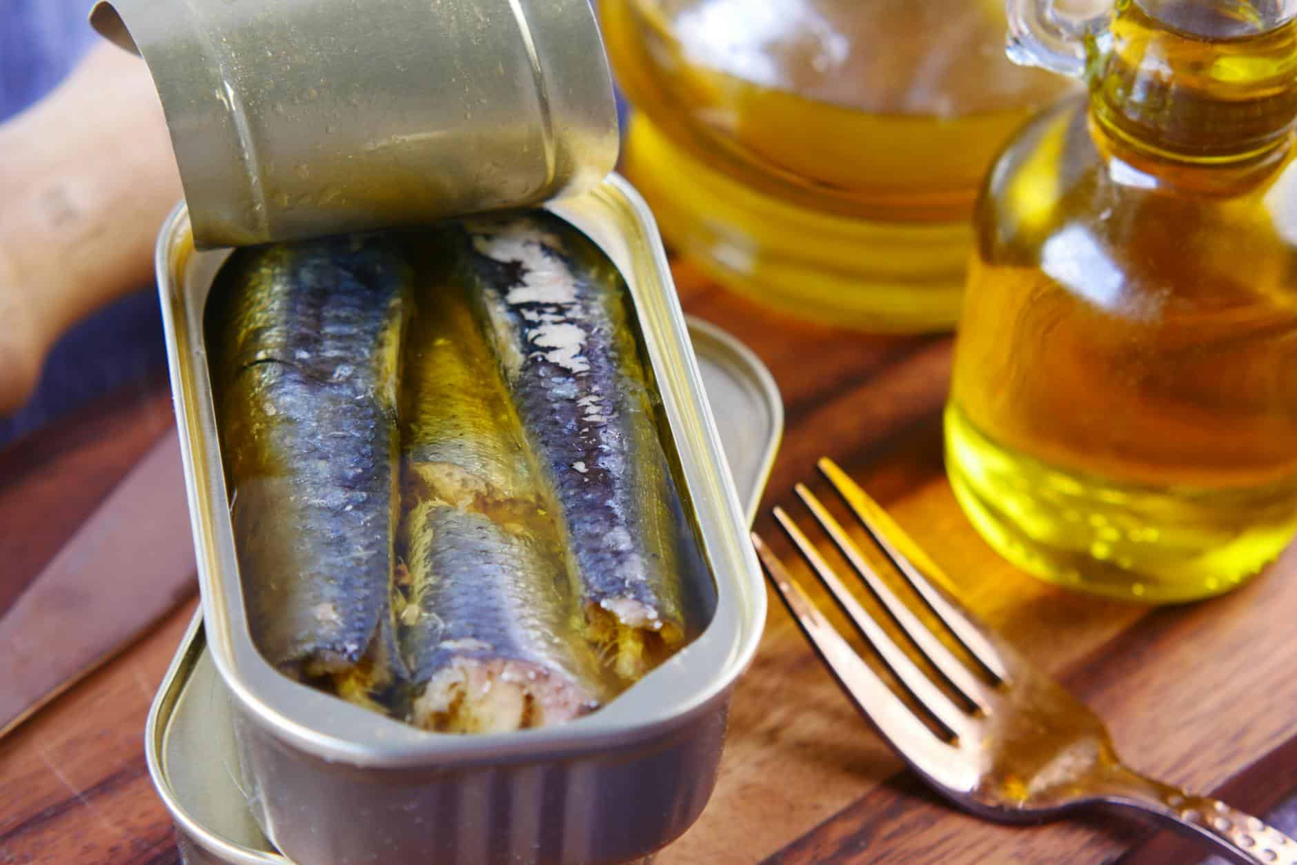 Close-up of canned sardines in olive oil with a fork on a wooden surface.