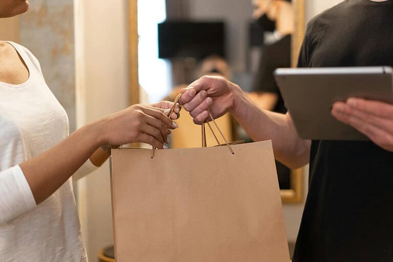 Close-up of hands exchanging a shopping bag indoors, symbolizing modern retail and technology