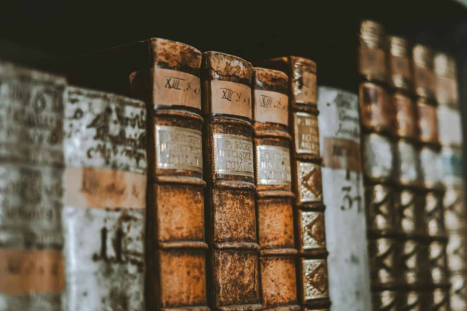 Close-up of vintage leather-bound books with classic spines in a dimly lit library.