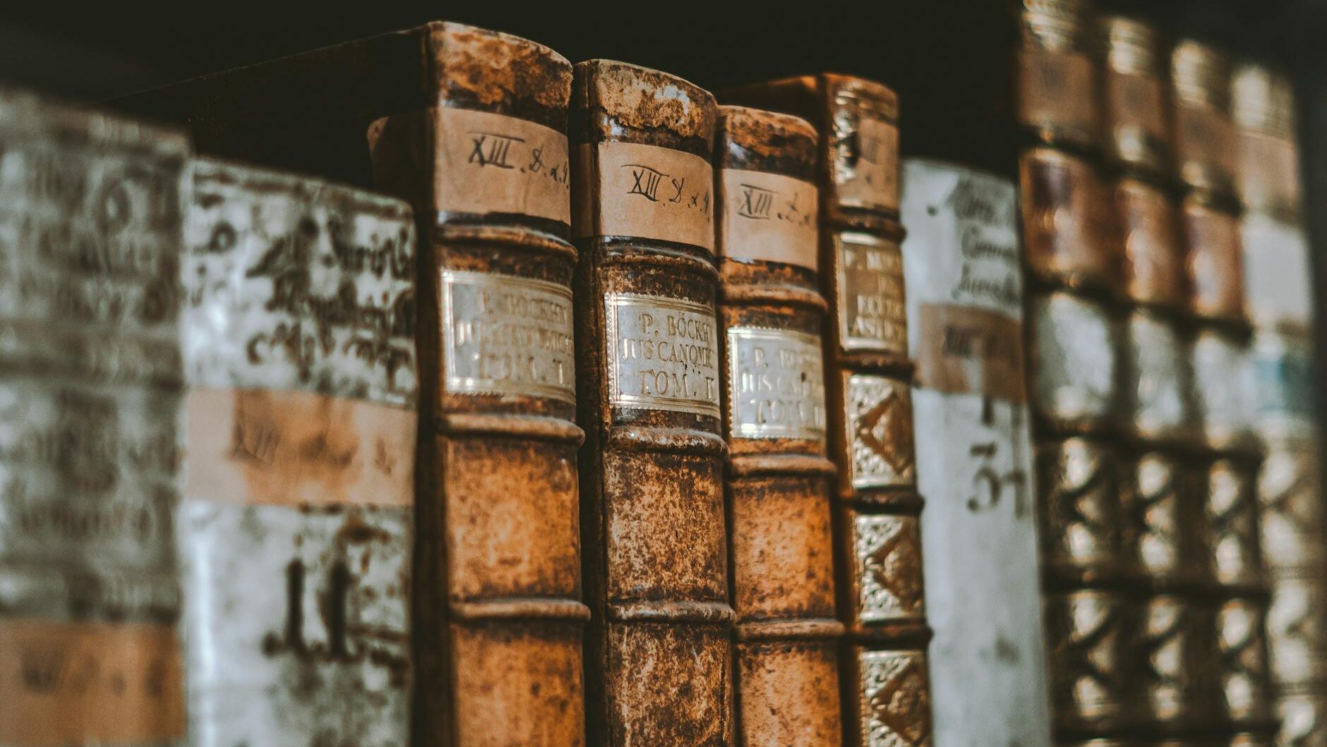 Close-up of vintage leather-bound books with classic spines in a dimly lit library.