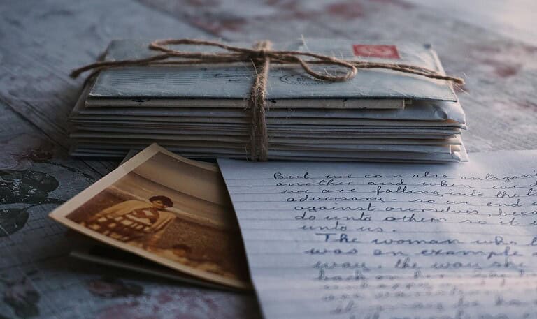 Close-up of vintage letters tied together with a twine, accompanied by an old photograph and handwritten note.