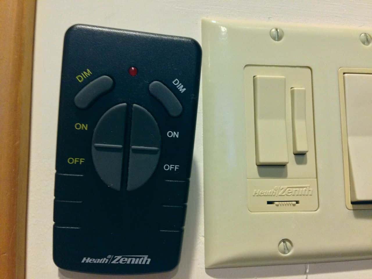The image shows a remote control dimmer switch mounted next to a standard light switch, the remote has buttons to turn the light on/off, dim the light, and adjust brightness