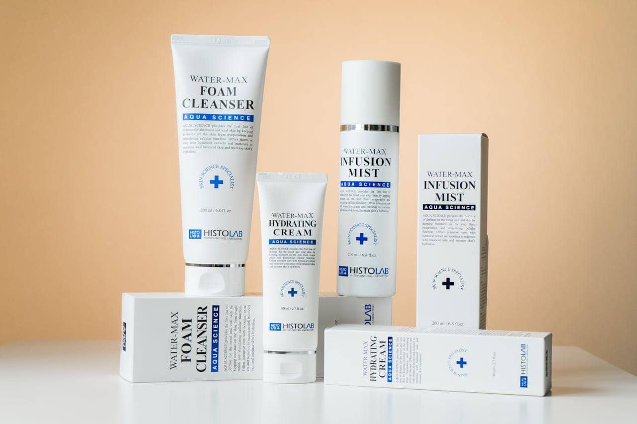 Collection of Histolab Water-Max skincare products against peach background, including foam cleanser, hydrating cream, infusion mist, with white packaging featuring blue medical cross logo and Aqua Science branding