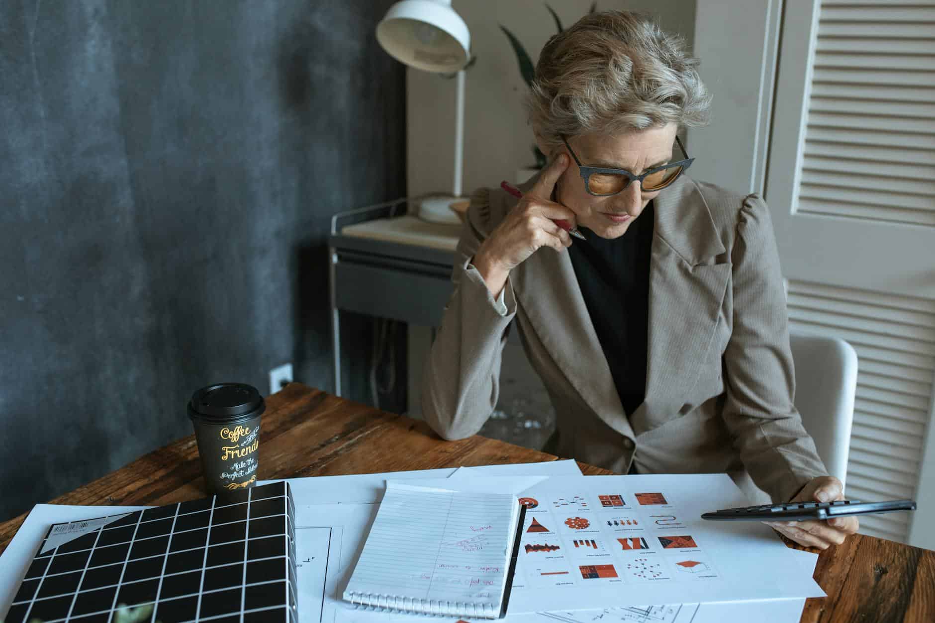 Focused businesswoman reviewing documents at desk in modern home office setting.