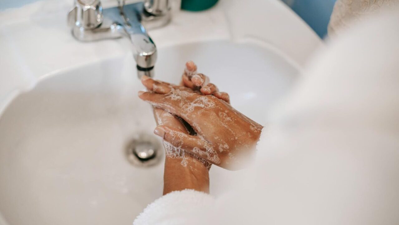 From above of crop unrecognizable ethnic female in robe washing hands with soap in bathroom