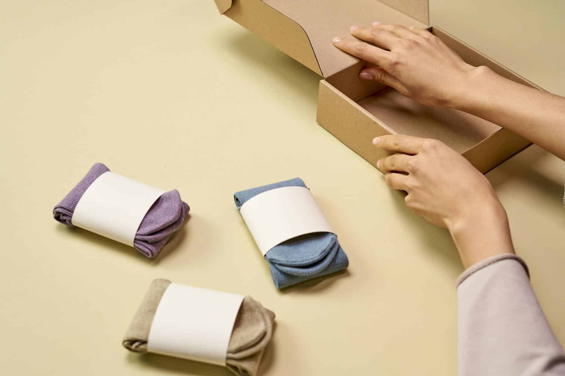 Hands packaging colorful socks into a cardboard box for shipment or storage.